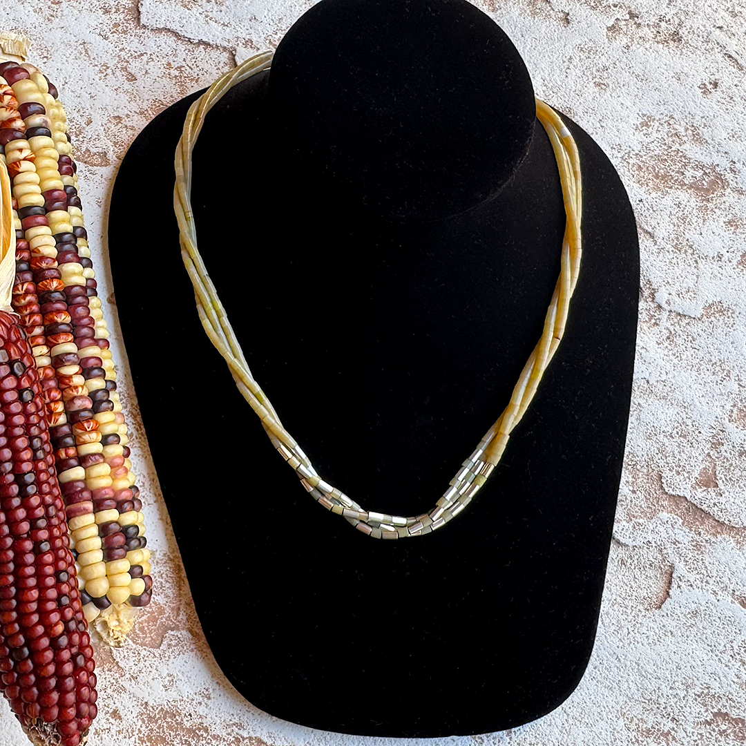 Necklace on a black velvet stand with corn cobs on a textured surface Pueblo handmade three strand yellow serpent sterling silver necklace in natural light setting